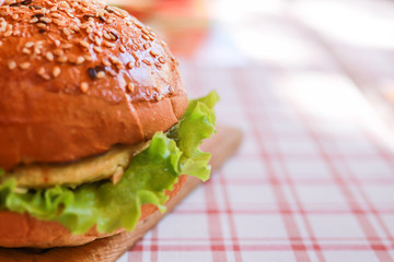 Close-up vegetarian burger with sesame seeds, artificial meat, green lettuce on the tablecloth.  Selected focus
