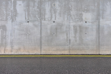 Concrete gray wall and asphalt road with a yellow line