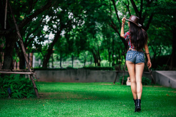 Full-length portrait of sexy young woman in cowboy hat, plaid shirt and denim shorts standing...