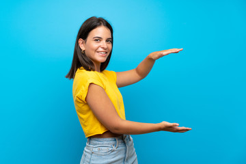 Young girl over isolated blue background holding copyspace to insert an ad