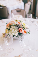 Fine wedding floral arrangement with pink peonies, white roses, dusty miller, and greenery, silver vase, white tablecloth, luxury wedding reception decor