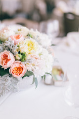 Fine wedding floral arrangement with pink peonies, white roses, dusty miller, and greenery, silver vase, white tablecloth, luxury wedding reception decor