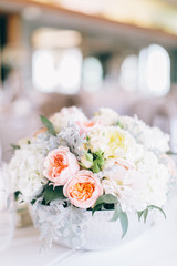 Fine wedding floral arrangement with pink peonies, white roses, dusty miller, and greenery, silver vase, white tablecloth, luxury wedding reception decor
