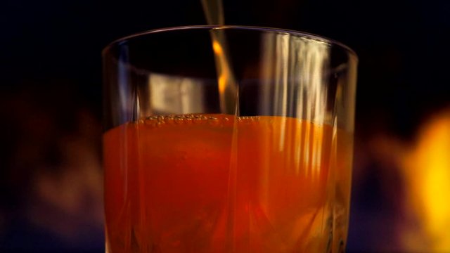 A yellow-orange sweet multifruit juice is poured into a glass with ice cubes. Glass with juice on a background of colored smoke.