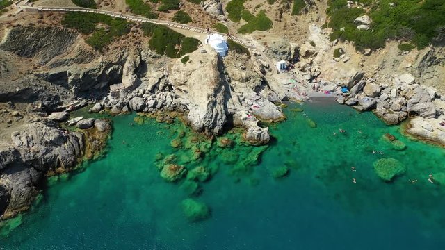Aerial drone video of iconic small chapel of Agia Anna built just above emerald rocky pebble beach, Amorgos island, Cyclades, Greece