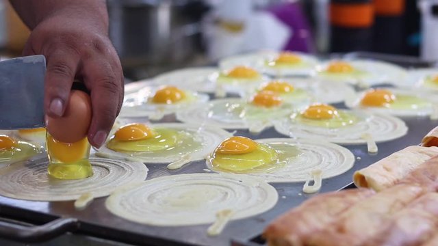 Male Asian Chef Cracking Chicken Eggs Onto A Hotplate