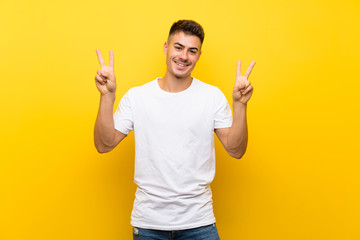 Young handsome man over isolated yellow background showing victory sign with both hands