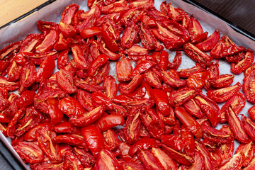 Homemade dried red  tomatoes slices with basil oregano spices cooking process. Traditional Italian Mediterranean kitchen cuisine.