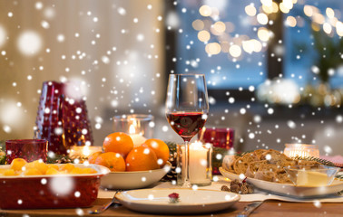 christmas dinner and eating concept - glass of red wine and food on table at home over snow