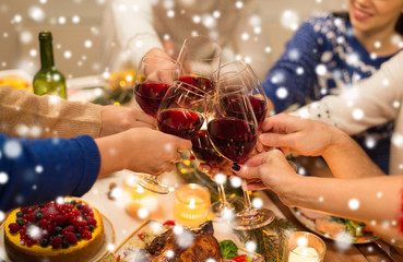 holidays and celebration concept - close up of happy friends having christmas dinner at home, drinking red wine and clinking glasses over snow