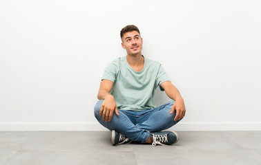 Fototapeta premium Young handsome man sitting on the floor laughing and looking up