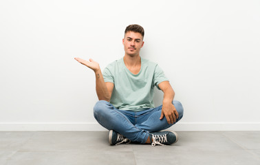 Young handsome man sitting on the floor holding copyspace imaginary on the palm