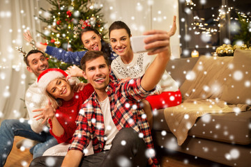 Obraz na płótnie Canvas celebration and holidays concept - happy friends with glasses celebrating christmas at home party and taking selfie by smartphone over snow