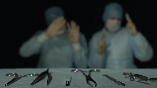 Doctors dance before or after operation or procedure in hospital. Funny and comic situation. Focus on surgical instruments lying in foreground. Successful hours-long surgery completed