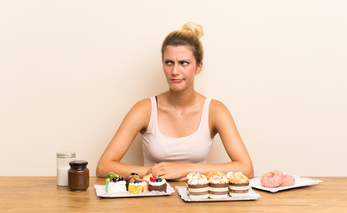 Young woman with lots of different mini cakes in a table standing and looking to the side