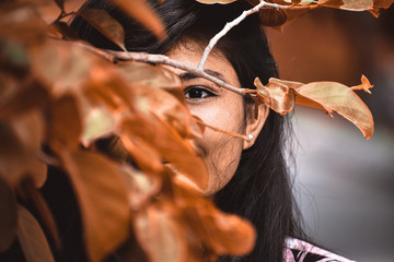 Portrait of Indian girl hiding face behind Orange leaves. Concept of skin care, organic cosmetics.