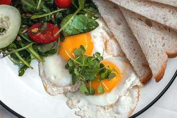 Two sunny side up eggs served with mixed season fresh salad and toasts, on a table outside of cafe or restaurant. Close-up top view. Tropical vacations concept.