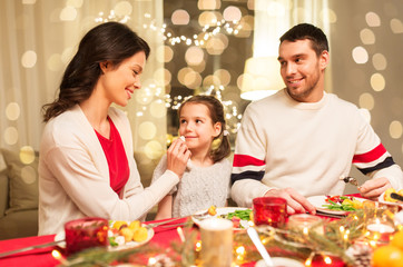holidays, family and celebration concept - happy mother, father and little daughter having christmas dinner at home