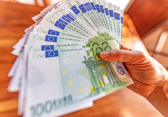 Mano femminile che tiene un mazzo di banconote da cento euro per migliaia di euro, guadagni e ricchezza facile - obrazy, fototapety, plakaty