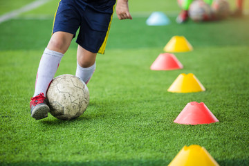 Kid soccer player jogging and control ball between cone markers on green artificial turf for soccer...