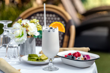 Tall Glass of vanilla milkshake smoothie with straw, slice of orange and blueberry. Tropical summer vacations concept.