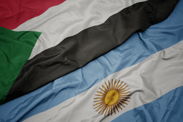 waving colorful flag of argentina and national flag of sudan.
