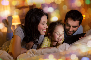 people and family concept - happy mother, father and little daughter with tablet pc computer in bed at night at home