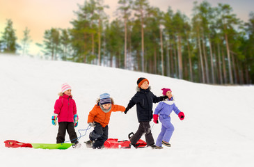 childhood, sledging and season concept - group of happy little kids with sleds over winter forest background