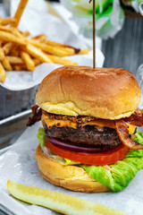 Tasty craft beef burger - juicy blue cheese cheeseburger with onions, slice tomato, lettuce, bacon, pickle and potato french fries at swimming pool. Tropical vacations concept. Fast food hamburger