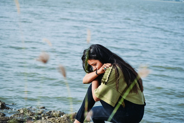 Beautiful Indian girl with black long hair sitting in front of lake. Nyari dam, Rajkot, India.