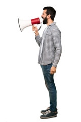 Handsome man with beard shouting through a megaphone over isolated white background