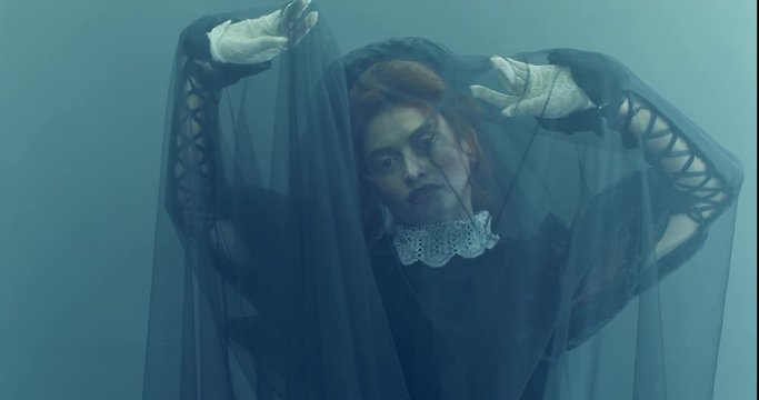 A red-haired woman in a black vintage dress, looking like a dead bride. Halloween. Horrors.