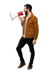 Handsome man with beard shouting through a megaphone over isolated white background