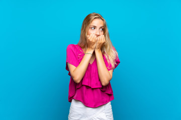 Blonde young woman over isolated blue background nervous and scared putting hands to mouth