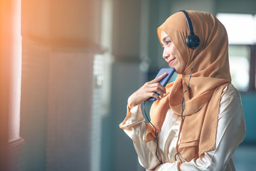 Portrait of a smiling young modern arabian woman holding mobile phone and listening the music to headphone.