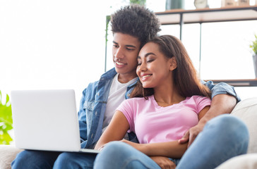 Smiling african teen couple relaxing and watching movie on laptop