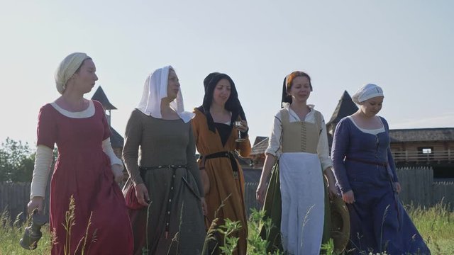 Medieval women going on camera at wooden fortress background. Clothes of medieval woman of 14-15 century.