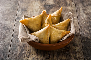 Samsa or samosas with meat and vegetables in bowl on wooden table. Traditional Indian food