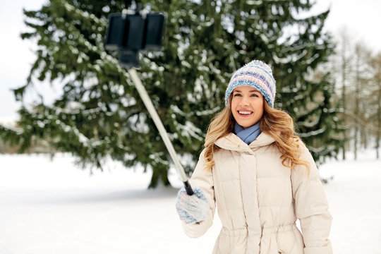 people, season and leisure concept - happy smiling woman taking picture by selfie stick in winter