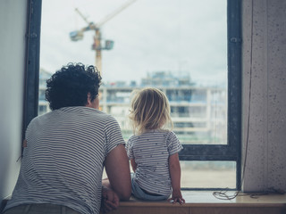 Father and toddler looking out the window of city apartment