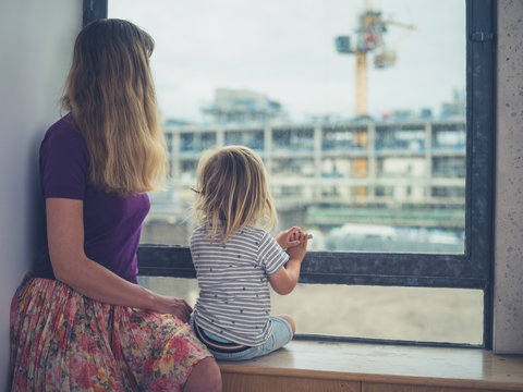 Mother and toddler looking out the window of city apartment