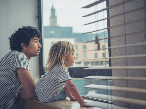Father and toddler looking out the window of city apartment