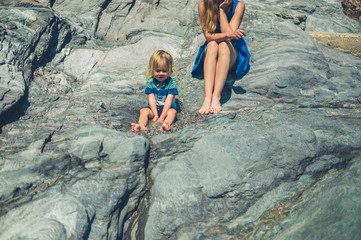 Young mother and toddler sitting on rocks in summer