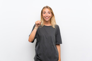 Blonde young woman over isolated white background surprised and pointing front