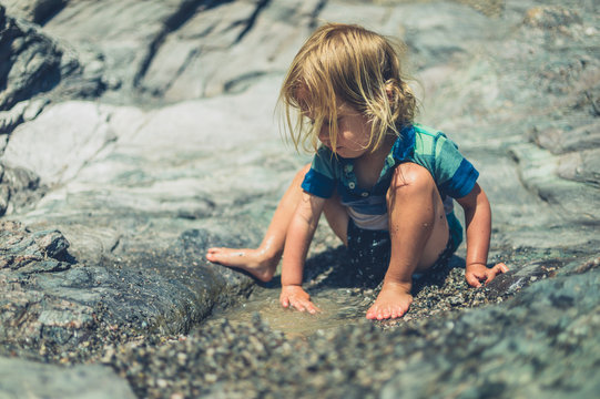 Little toddler playing with water on rocky beach