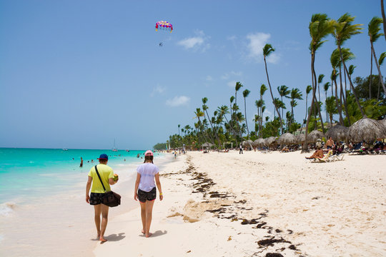 Teenagers walking along sandy beach, parasail wing in the background, Punta Cana, Dominican Republic