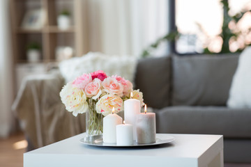 decoration, hygge and cosiness concept - candles burning on table and flowers at cozy home