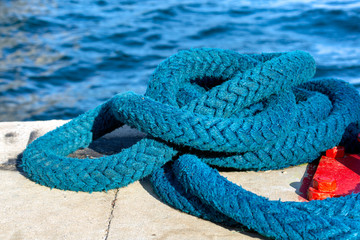 Blue colored aged boat manila rope placed on a concrete road at the port. Sea in the background.