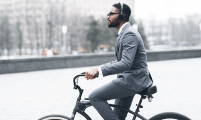Afro businessman with headphones riding on bicycle to work