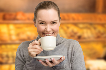 Young woman with a cup of fresh coffee in her hand and bakery in background 